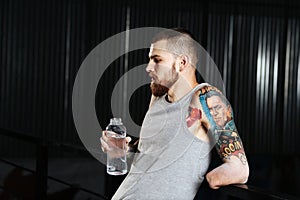 Tired disabled armless young man leaning back on a metal railing, drinking water