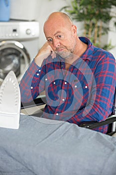 Tired disabled man with iron and ironing board