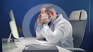 Tired doctor in a medical office at a work desk in front of a computer