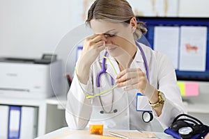 Tired doctor siting at table in his office and looks after his eyes