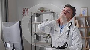 Tired doctor sits in front of the monitor and massages his face and neck 4k slow motion movie