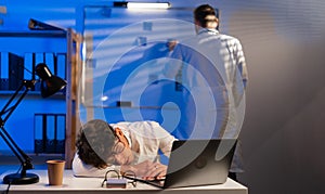 Tired doctor sleeping at the table during the night shift in the hospital and his colleague working with documents