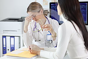 Tired doctor taking off glasses in front of patient in clinic