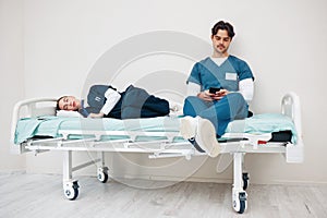 Tired doctors, woman and man in hallway with phone, texting and relax on bed at hospital job. Medic team, partnership or