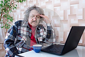Are tired elderly man with a headache after a long work at the laptop is sitting