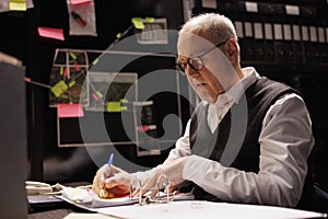 Tired elderly police officer sitting at desk in evidence room