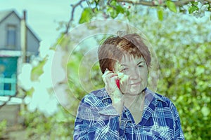 Tired elderly woman at the dacha talking on a cell phone