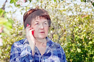 Tired elderly woman at the dacha talking on a cell phone