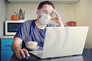 A tired employee works from a home office. young man wearing medical face mask at work from home office due to corona photo