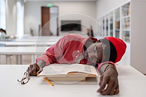 Tired exhausted African guy student falling asleep while studying in library