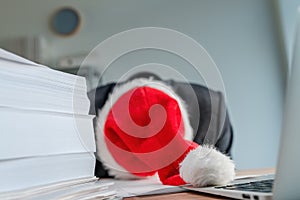 Tired and exhausted businessman with Santa Claus hat fell asleep over his desk during Christmas