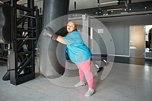 Tired exhausted fat woman leaning and hugging punching bag while training in gym