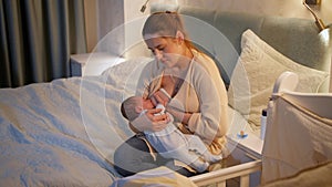 Tired and exhausted mother falling asleep while feeding her newborn baby son with breast milk on bed at night. Concept