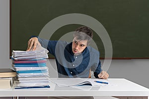 Tired and exhausted teacher is correcting many exams in classroom
