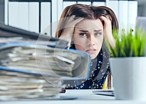Tired and exhausted woman looks at the mountain of documents propping up her head with her hands.