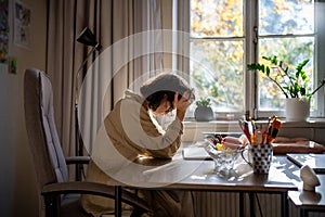 Tired exhausted woman sitting at table holding head early morning after working all night.