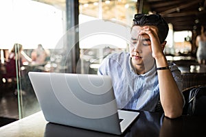 Tired exhausted young asian male working with laptop in cafe. Freelance work
