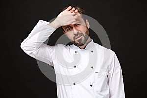 Tired exhausted young bearded male chef cook or baker man in white uniform shirt posing isolated on black wall