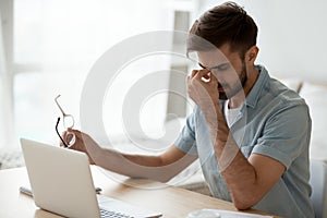 Stressed fatigued young man taking off glasses feeling eyestrain headache