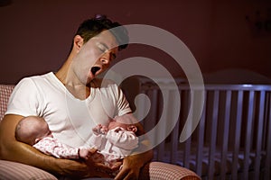 Tired Father At Home Cuddling Twin Baby Daughters In Nursery