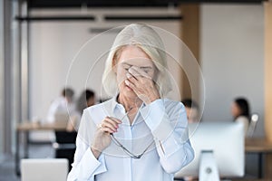 Tired fatigued senior female employee taking off glasses feeling eyestrain
