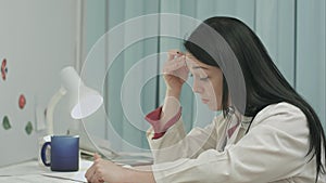 Tired female doctor sits in a medical office in the clinic and writes diagnose of patient