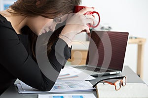 Tired female employee at workplace in office holding cup of tea