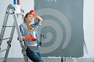 Tired female house painter with roller paints wall