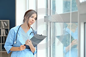 Tired female nurse near window in hospital