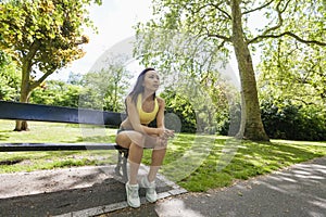 Tired fit woman sitting on beach while exercising in park