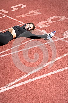 Tired fit woman in sportswear resting after workout or running on a treadmill rubber stadium, holding a bottle of water, taking a