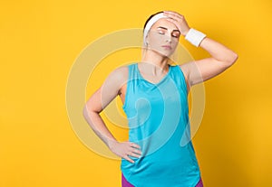Tired fitness woman resting after workout at gym, keeps hand on forehead. Sport female taking break after training session,