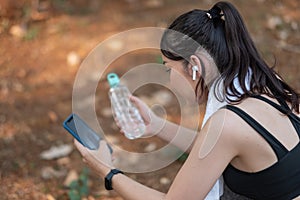 Tired fitness woman sweating taking a break listening to music on phone after difficult training