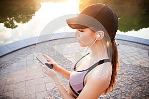 Tired fitness woman sweating taking a break listening to music on phone after difficult training. Young woman listening