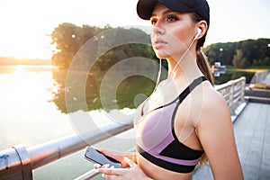 Tired fitness woman sweating taking a break listening to music on phone after difficult training. Young woman listening
