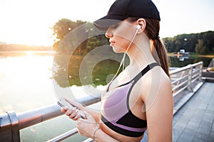 Tired fitness woman sweating taking a break listening to music on phone after difficult training. Young woman listening