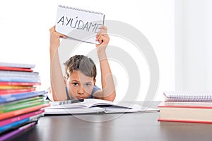 Tired frustrated boy sitting at the table with many books, exercises books. Spanish word Auydame - Help me- is written photo