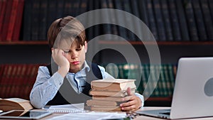Tired frustrated male kid schooler sleeping with stack of textbook on table at public library