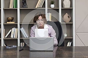 Tired frustrated and overworked business woman sitting in the office, holding documents and reading about problems in business