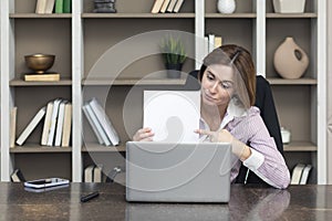 Tired frustrated and overworked business woman sitting in the office, holding documents and reading about problems in business