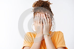 Tired girl hiding face unwilling everyone see cry, cover eyes palms wearing glasses orange t-shirt, playing peek-a-boo