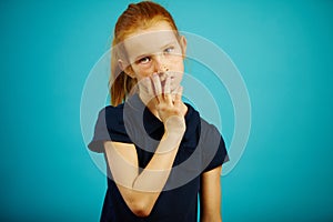 Tired girl puts her hand to her face, expresses fatigue and weariness, stands on blue isolated background. Sleepy child