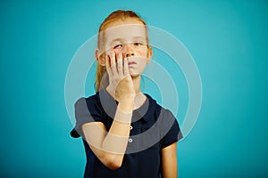 Tired girl puts her hand to her face, expresses fatigue and weariness, stands on blue isolated background. Sleepy child