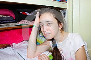 A tired girl stands near the wardrobe after cleaning, her head propped on her hand