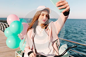 Tired girl with a stylish make-up is photographed at the sea background after morning bike ride along the pier. Gorgeous