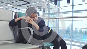 Tired girl teen in headphones traveler sleeping on the airport waiting for the plane departure gates bench with all her