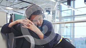 Tired girl teen in headphones traveler sleeping on the airport waiting for the plane departure gates bench with all her