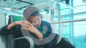 Tired girl teen in headphones traveler sleeping on the airport waiting for the plane departure gates bench with all her