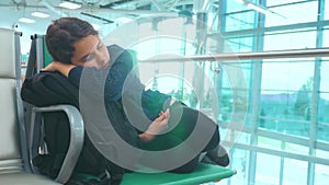 Tired girl teen traveler sleeping on the airport waiting for the plane departure gates bench with all her luggage by her