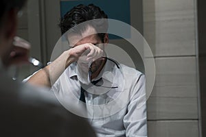 Tired handsome businessman standing in front of mirror in the restroom after exhausting busy workday